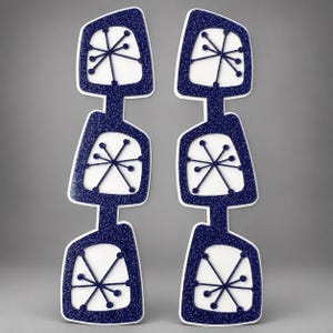 May include: Two vertical wall decorations featuring three stacked, irregular quadrilateral frames in dark blue glitter. Each frame contains a white center with a dark blue starburst pattern consisting of thin lines and small circular endpoints.