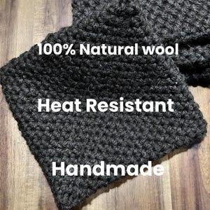 May include: Close-up of a dark grey, handmade wool item. The text on the item reads "100% Natural wool", "Heat Resistant", and "Handmade". The item has a textured, woven appearance.