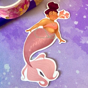 May include: A pink mermaid sticker with a crown of seaweed and a small orange fish. The mermaid has brown hair and is blowing a kiss.