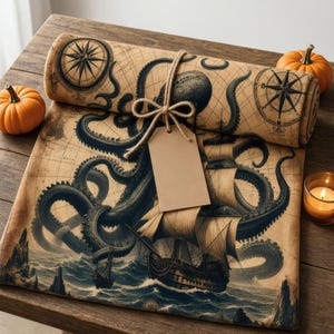 Op de afbeelding: Een opgerolde stof met een vintage kaartprint met een grote donkere octopus, een zeilschip en kompasrozen. De stof is vastgebonden met een bruin touwtje en een leeg rechthoekig papieren label, geaccentueerd door twee kleine oranje pompoenen.