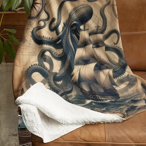 May include: A beige throw blanket featuring a vintage map design with a large octopus attacking a sailing ship. The blanket has a white, fluffy underside and is draped over a brown leather couch.