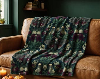 Op de afbeelding: Een donkergekleurde plaid met een herhalend patroon van motten met rode en witte markeringen, afgewisseld met diepgroen gebladerte en donkerpaarse florale elementen. De stof vertoont een dicht, op de plantkunde geïnspireerd ontwerp.