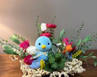 Arreglo floral de Pascua con pájaro azul, huevos en tonos pastel y decoración rústica para mesa.