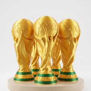 Könnte beinhalten: Mehrere goldfarbene FIFA-Weltpokal-Trophäen werden auf einem hellen Holzsockel präsentiert. Die Trophäen haben ein Globus-Design, das von zwei Figuren gehalten wird. Der Sockel jeder Trophäe ist grün mit der Aufschrift "FIFA WORLD CUP".