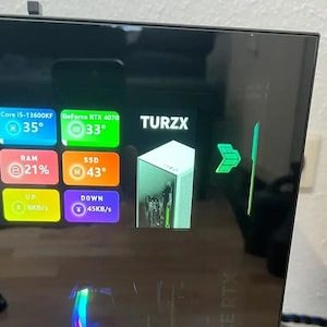 May include: A computer monitor displaying system information. The screen shows the text "TURZX" and temperature readings for the CPU, GPU, RAM, and SSD. The graphics card is a GeForce RTX 4070. The monitor also displays upload and download speeds.