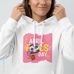Può includere: Felpa con cappuccio bianca con una grafica colorata. La grafica presenta la scritta "APRIL FOOLS DAY" con occhi, naso e baffi dei cartoni animati. È inclusa anche una piccola scatola rossa con una faccia.