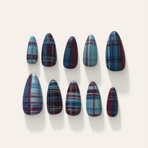 May include: A collection of ten false nails, each with an almond shape. The nails display a plaid design in blue, burgundy, and white. They are presented on a white background, highlighting the pattern and form.
