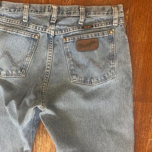 Puede incluir: Vaqueros de mezclilla azul claro con el logotipo de Wrangler en el bolsillo trasero. Los vaqueros tienen un estilo cl&aacute;sico de cinco bolsillos, trabillas para el cintur&oacute;n y cierre de bot&oacute;n y cremallera. La mezclilla tiene un aspecto descolorido.
