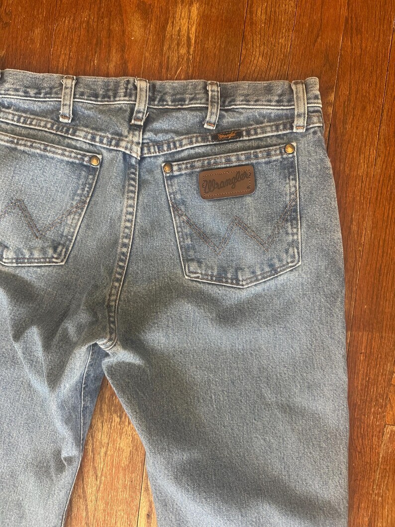 Puede incluir: Vaqueros de mezclilla azul claro con el logotipo de Wrangler en el bolsillo trasero. Los vaqueros tienen un estilo cl&aacute;sico de cinco bolsillos, trabillas para el cintur&oacute;n y cierre de bot&oacute;n y cremallera. La mezclilla tiene un aspecto descolorido.