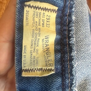 Puede incluir: Primer plano de una etiqueta de vaqueros de mezclilla azul. La etiqueta dice "WRANGLER NO-FAULT DENIM" con la talla 29x32. La etiqueta tambi&eacute;n incluye instrucciones de lavado y "MADE IN U.S.A."