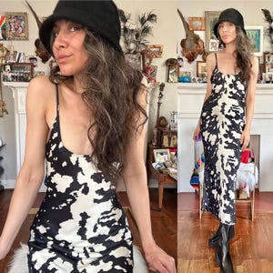 May include: A black and white patterned slip dress with spaghetti straps. The dress has a cow print design and is paired with black boots and a black hat. The dress is knee-length and form-fitting.