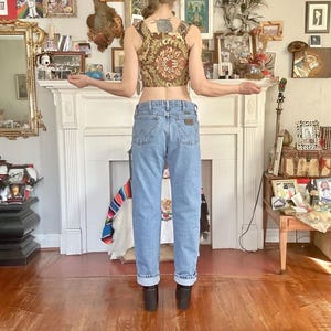 Puede incluir: Un top corto con estampado floral en tonos marr&oacute;n, dorado y rojo, combinado con vaqueros de mezclilla azul claro. Los vaqueros tienen un corte cl&aacute;sico. La persona lleva botines negros.
