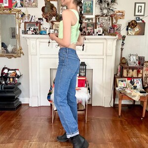 Puede incluir: Un top corto verde claro con dobladillo con volantes y vaqueros azules. Los vaqueros est&aacute;n doblados en los tobillos. La persona lleva botas negras y una gorra de b&eacute;isbol negra.