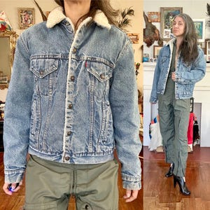 Puede incluir: Chaqueta vaquera de lavado claro con cuello y forro de borreguillo blanco y esponjoso. La chaqueta tiene dos bolsillos en el pecho, cierres de botón y una etiqueta roja con el logo. La chaqueta se usa con pantalones cargo verde oliva.