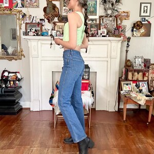 Puede incluir: Un top corto acanalado verde claro combinado con jeans azules y botas negras. El atuendo se completa con una gorra de b&eacute;isbol negra. La modelo est&aacute; en una habitaci&oacute;n con chimenea y varios objetos decorativos.