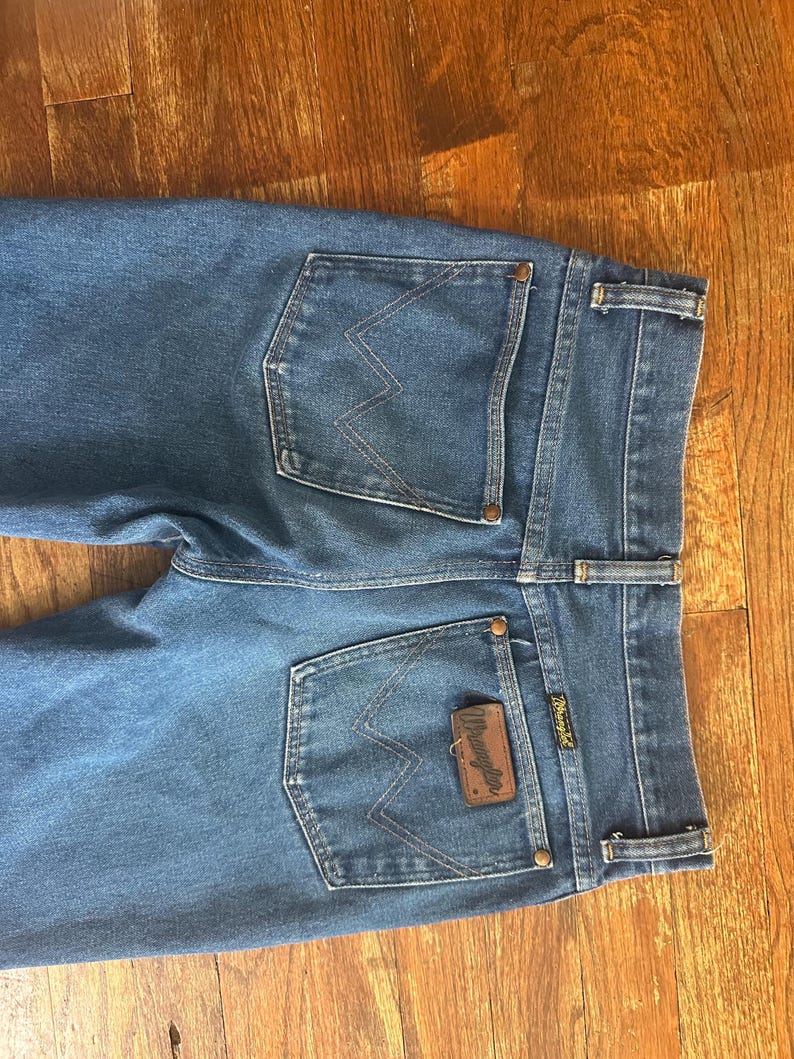 Puede incluir: Vaqueros azules de mezclilla con el logo de Wrangler en el bolsillo trasero. Los vaqueros tienen un estilo cl&aacute;sico de cinco bolsillos con corte recto. Los bolsillos traseros presentan las costuras distintivas de Wrangler.