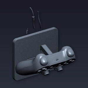 May include: A grey video game controller mounted on a grey rectangular base. The controller features multiple buttons and joysticks. Cables and a connector are also visible, suggesting a charging or connection setup. The background is a dark grey.