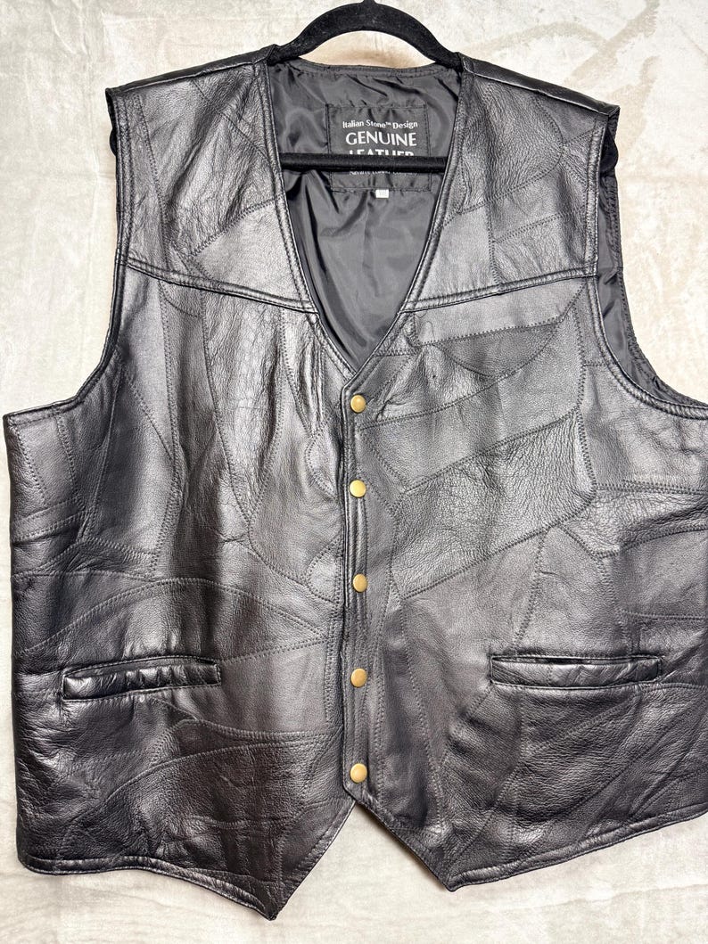 May include: A black leather waistcoat featuring a patchwork design of stitched leather panels, a V-neckline, and five brass-coloured snap buttons. The interior label reads Italian Stone Design GENUINE LEATHER. The waistcoat includes two front slit pockets.
