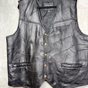 May include: A black leather waistcoat featuring a patchwork design of various leather pieces. The waistcoat has a V-neckline, five gold-toned metal snap buttons down the front, and two horizontal slit pockets. A label inside reads Italian Stone Design GENUINE.