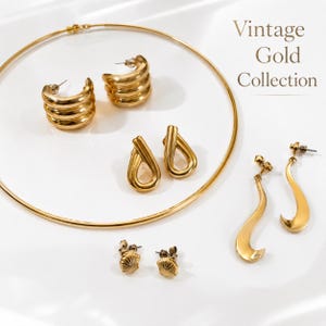 Könnte beinhalten: Ein goldfarbenes Schmuckset bestehend aus einem dünnen, kreisförmigen Halsreif und vier Paar Ohrringen: gerippte Creolen, tropfenförmige Stecker, muschelförmige Stecker und lange, geschwungene Hängeohrringe. Der Text Vintage Gold Collection ist sichtbar.