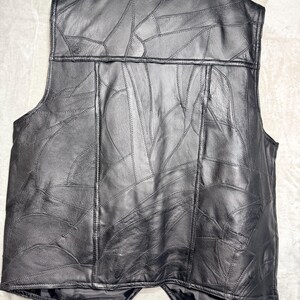 May include: A black leather waistcoat featuring a patchwork design composed of numerous irregularly shaped leather pieces stitched together. The waistcoat has a sleeveless construction, a round neckline, and a straight hemline with a slight V-shape at the centre.