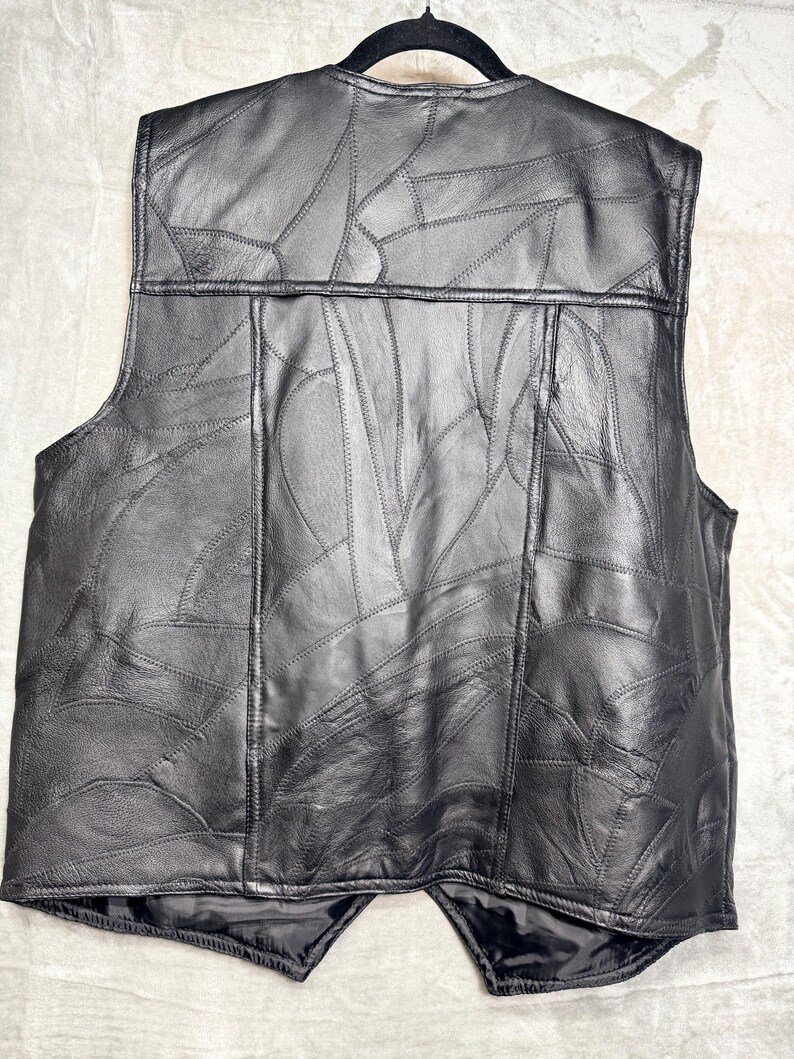 May include: A black leather waistcoat featuring a patchwork design composed of numerous irregularly shaped leather pieces stitched together. The waistcoat has a sleeveless construction, a round neckline, and a straight hemline with a slight V-shape at the centre.