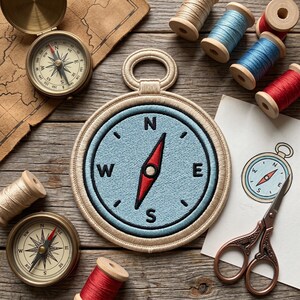 May include: A collection of nautical-themed items on a wooden surface. Includes a large embroidered compass patch, two antique compasses, spools of thread in various colors, and a small drawing of a compass. A pair of decorative scissors is also present.
