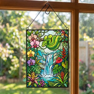 May include: A rectangular stained glass suncatcher featuring a green snake coiled on a branch above a waterfall. The scene includes vibrant tropical flowers, including pink, yellow, and purple orchids, red anthuriums, and lush green foliage.