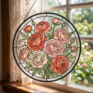 May include: A circular stained glass suncatcher featuring a bouquet of ranunculus flowers in shades of coral, peach, and cream. The design includes green leaves and stems, all encased in a black metal frame with a hanging chain attached at the top.