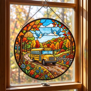 May include: A circular stained glass suncatcher featuring a yellow school bus labeled "SCHOOL BUS" and "AUTUMN TOURS" driving on a road through a forest with orange, red, and yellow autumn leaves, blue sky, white clouds, and two blue birds.