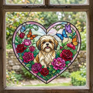 May include: A heart-shaped stained glass suncatcher featuring a central illustration of a fluffy tan and white dog surrounded by vibrant red and pink roses, green leaves, and colorful butterflies in shades of blue, orange, and purple.