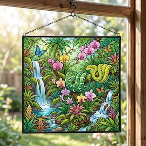 May include: A square stained glass panel featuring a tropical jungle scene with two green snakes, a cascading waterfall, vibrant pink and yellow orchids, and butterflies, all enclosed in a black metal frame with a hanging chain.