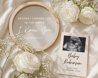 May include: A circular mirror with a wooden frame displays the text "BEFORE I FORMED YOU IN THE WOMB I KNEW YOU JEREMIAH 1:5". A card with a baby ultrasound image reads "Baby Robinson ARRIVING FEBRUARY 202X". White roses and baby's breath surround the items.