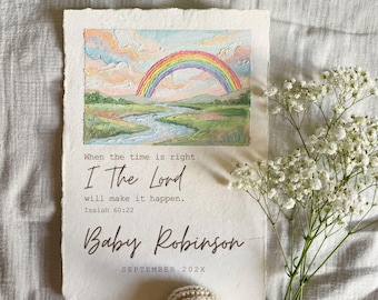 May include: A watercolor print featuring a rainbow over a river landscape. The text reads "When the time is right, I The Lord will make it happen. Isaiah 60:22" and "Baby Robinson, September 202X". The print is on textured paper.