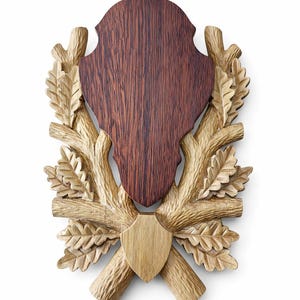 Puede incluir: Placa de madera con un centro marrón oscuro y un diseño de hojas y ramas de roble marrón claro. La placa tiene forma de escudo en la parte inferior y una parte superior decorativa.