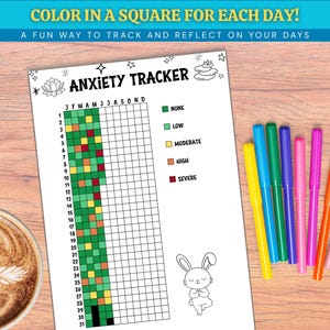 May include: A white Anxiety Tracker sheet with a grid for tracking emotions, accompanied by colorful markers. The sheet includes the text "COLOR IN A SQUARE FOR EACH DAY!" and "A FUN WAY TO TRACK AND REFLECT ON YOUR DAYS". A cup of coffee is in the background.