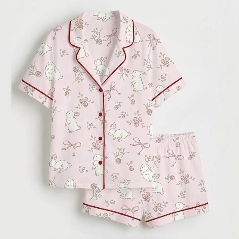 May include: A light pink pajama set with a pattern of white rabbits, pink roses, and bows. The short-sleeved top and shorts have burgundy trim. The set is made of a soft, lightweight fabric.