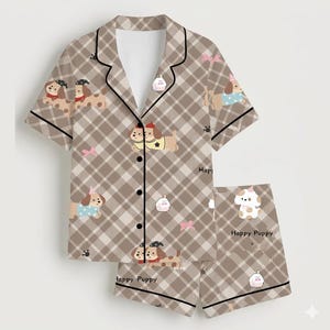 May include: A two-piece pajama set featuring a brown plaid pattern with cartoon puppies, bows, and small white objects. The short-sleeved top has black trim and buttons. The shorts have the text "Happy Puppy".