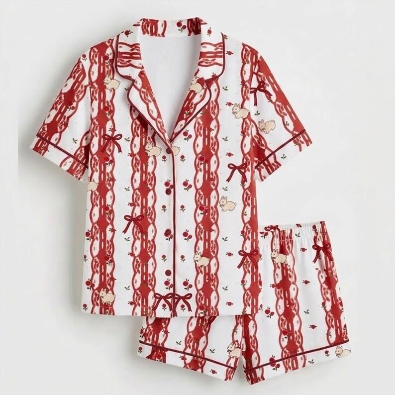 May include: A two-piece pyjama set. The white fabric is patterned with red vertical stripes, bows, and small animal illustrations. The short-sleeved top and shorts are trimmed in red.