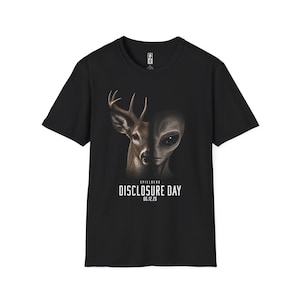 Op de afbeelding: Zwart T-shirt met een afbeelding van een hert en een alien gezicht. De tekst "DISCLOSURE DAY 06.12.26" staat onder de afbeelding. Het shirt heeft een ronde hals en korte mouwen.