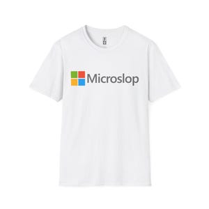Puede incluir: Camiseta blanca con la palabra "Microslop" en texto gris. La palabra está precedida por un logotipo cuadrado colorido con cuadrados verdes, rojos, naranjas y azules. La camiseta es de cuello redondo y manga corta.