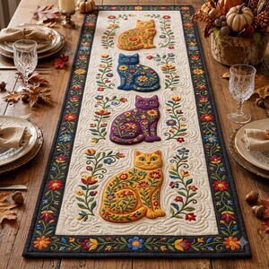 May include: A rectangular table runner featuring a cream-colored center panel with four embroidered cats in orange, blue, purple, and yellow, each decorated with floral patterns. The runner has a dark border with colorful embroidered flowers.