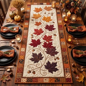May include: A rectangular quilted table runner featuring a central cream-colored panel with an embroidered vine pattern of autumn maple leaves in shades of orange, red, and dark purple, accented by small acorns and a patchwork border of plaid fabrics.