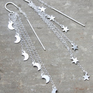 May include: Silver dangle earrings with multiple chains and crescent moon and star charms.