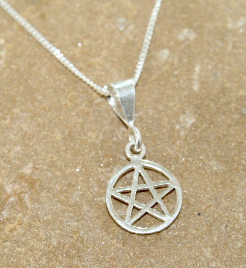 May include: A silver chain necklace with a silver pendant featuring a five-pointed star inside a circle.