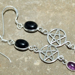 May include: Silver earrings with black and purple gemstones. Each earring features a silver pentagram charm.