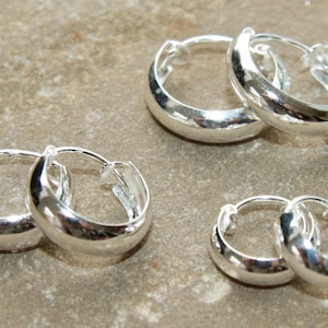 May include: Three pairs of silver hoop earrings of different sizes. The earrings are smooth and shiny.
