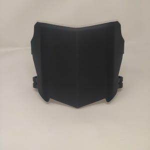 May include: A black, angular motorcycle fairing, designed to fit over the front of a motorcycle. The fairing has a smooth, matte finish and a distinctive shape with a central point and curved edges. It features mounting brackets on the sides.
