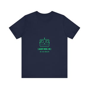 Pode incluir: T-shirt azul marinho com um gráfico de rosto de robô verde e o texto "[AGENT MODE: ON] do not disturb". O design está centrado na frente da camisa. A camisa é feita de um material macio e confortável.