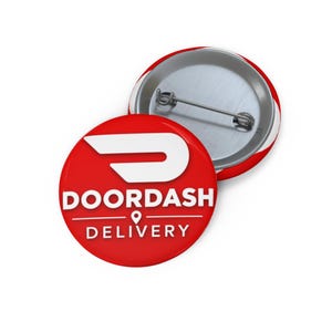 May include: A round pinback button featuring a vibrant red background with the white DoorDash logo and the text DOORDASH DELIVERY printed in white. The back of the button is metallic silver and includes a horizontal metal pin fastener mechanism.